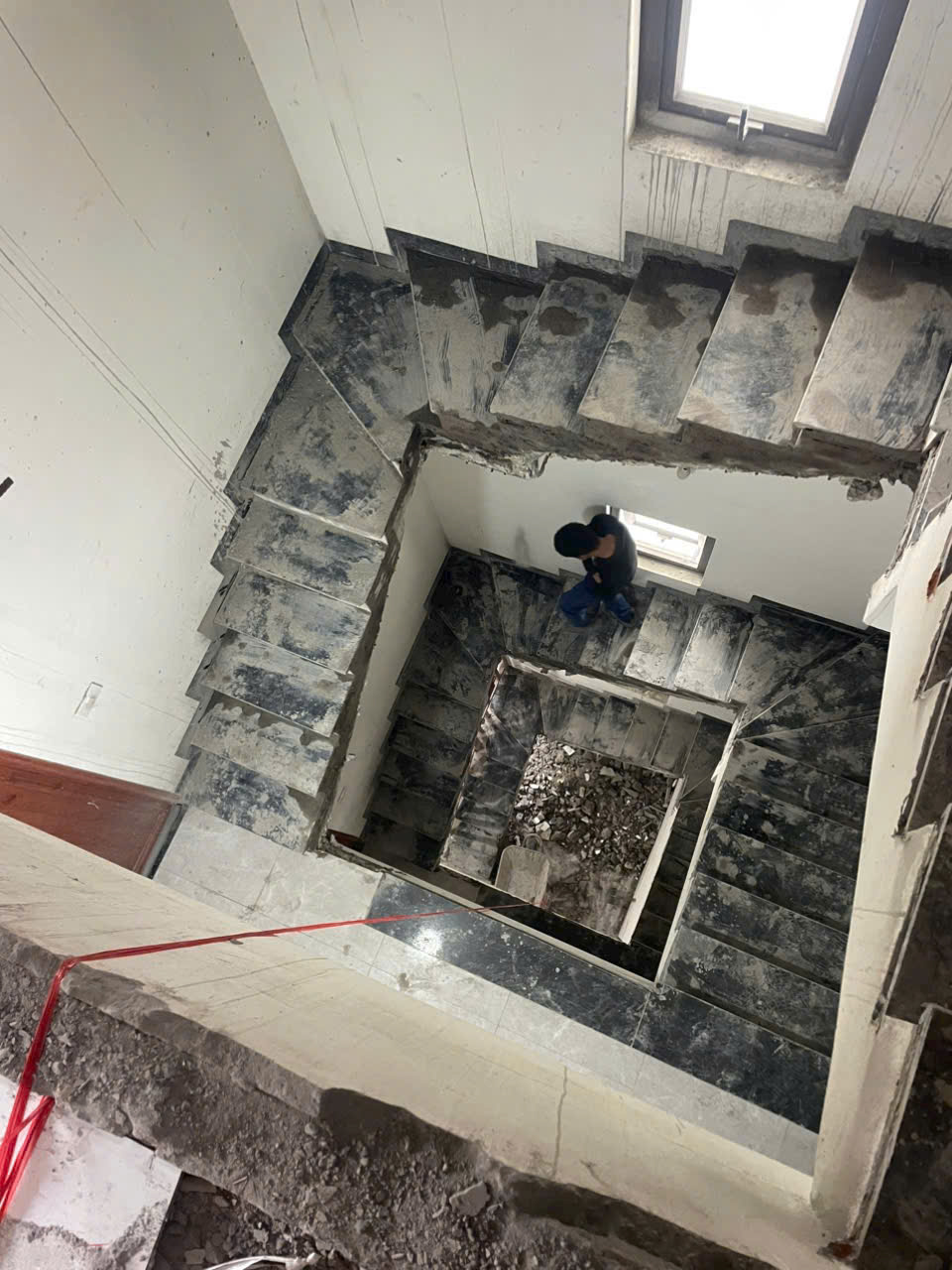 Cầu thang bê tông đang thi công dở, nhiều bụi bẩn và gạch vỡ, công nhân đứng ở tầng dưới